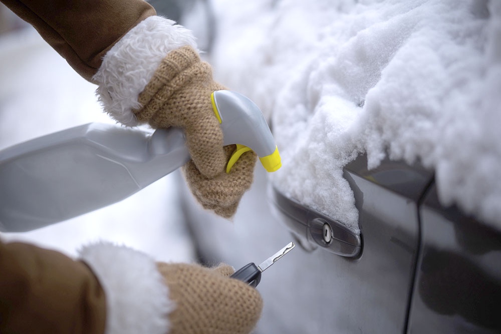 Рука в перчатке направляет струю аэрозоля-размораживателя в замерзшую личинку дверного замка автомобиля.