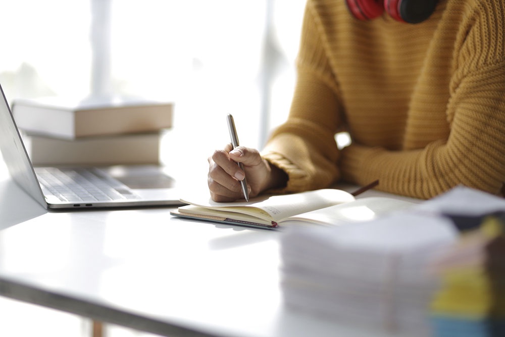 Школьник готовится к ЕГЭ по английскому дома, сидит за столом с учебниками, тетрадями и ноутбуком.