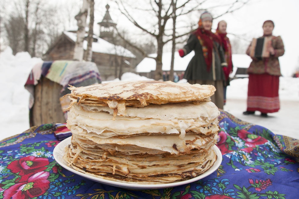 Стопка блинов  и люди празднующие Масленицу.