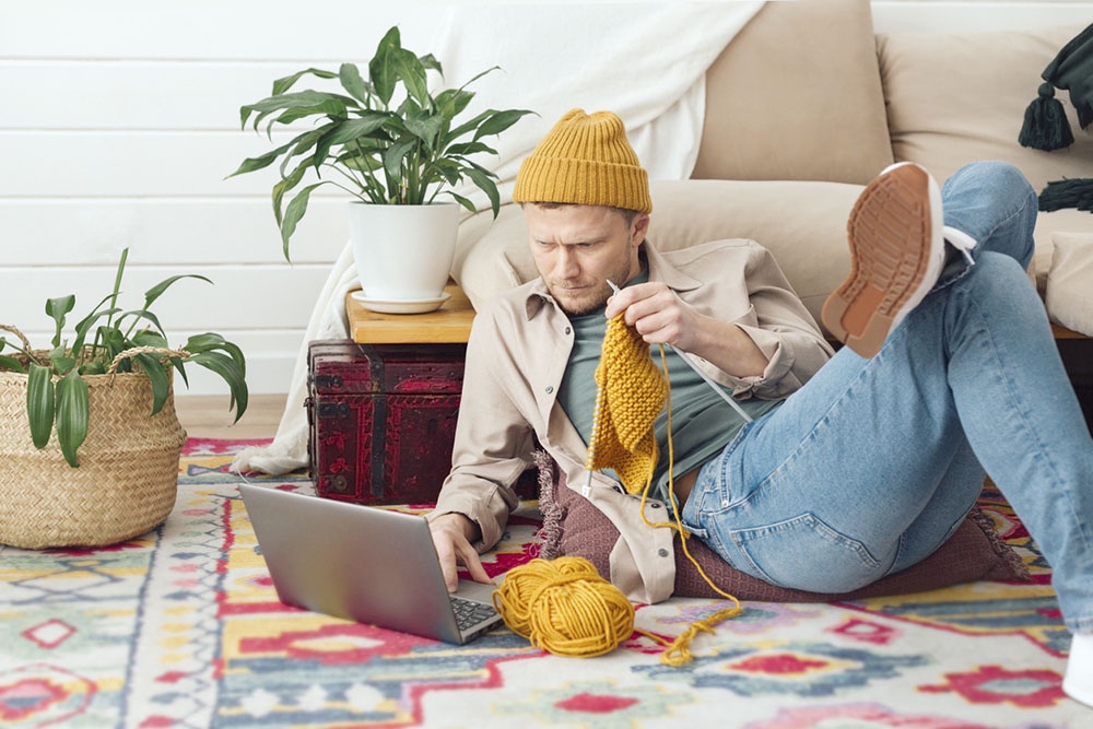 Мужчина осваивает новое хобби - вязание. Он вяжет длинный жёлтый шарф.