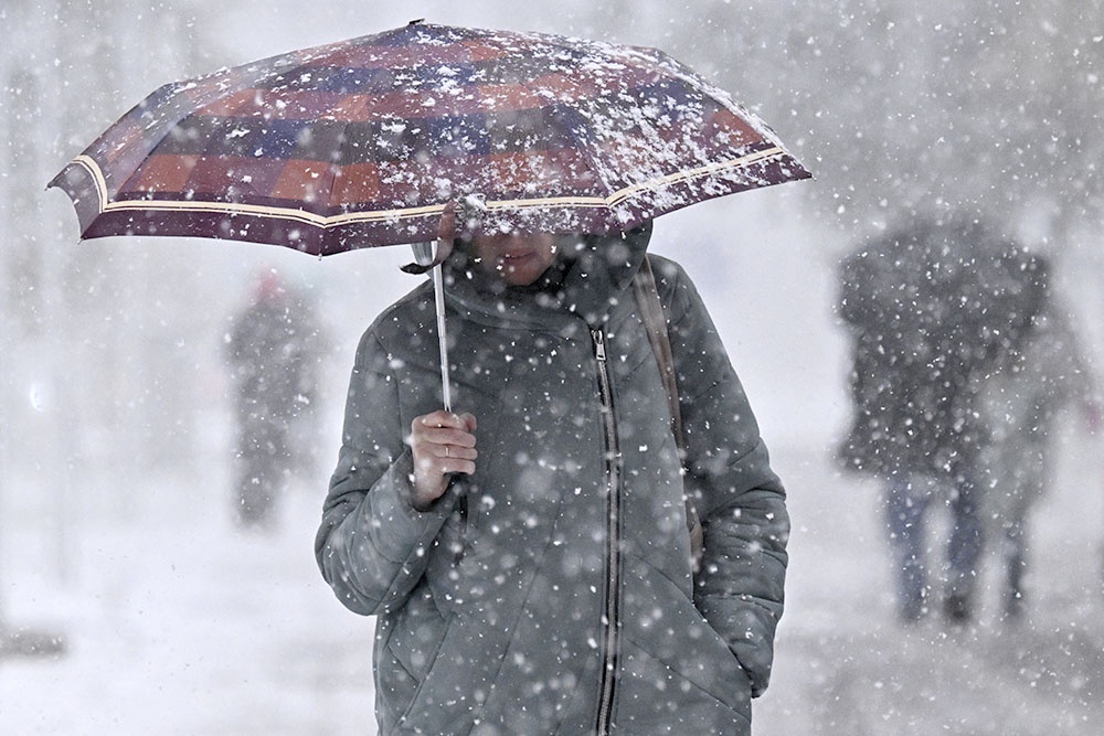 Человек идет под зонтом в сильный снегопад.