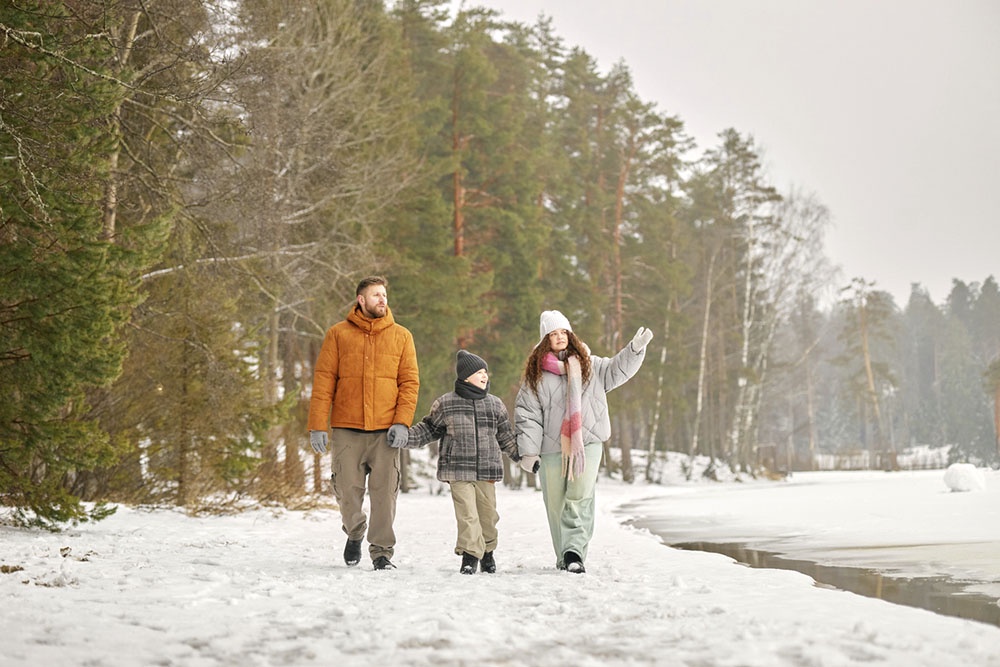 Семья гуляет по заснеженному берегу озера.