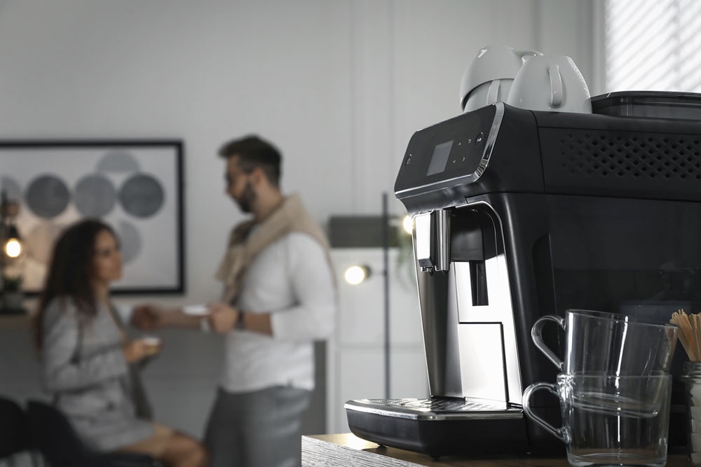 Мужчина и женщина пьют свежесваренный кофе на кухне, на переднем плане автоматическая кофемашина.