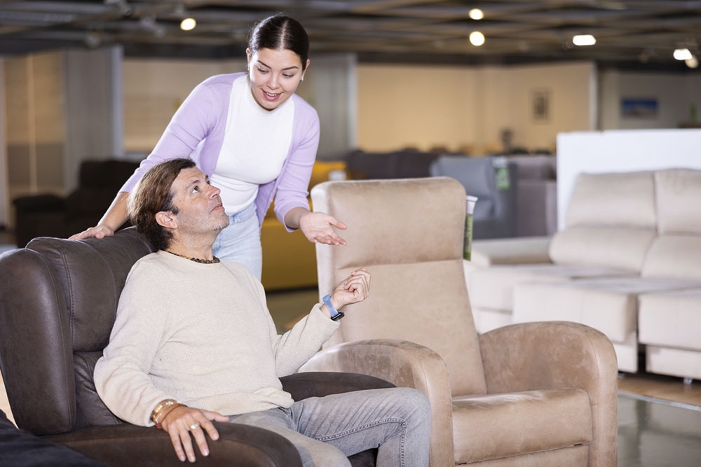 Пара в мебельном магазине: мужчина и женщина подбирают кресло для дома, тестируя комфорт и дизайн.