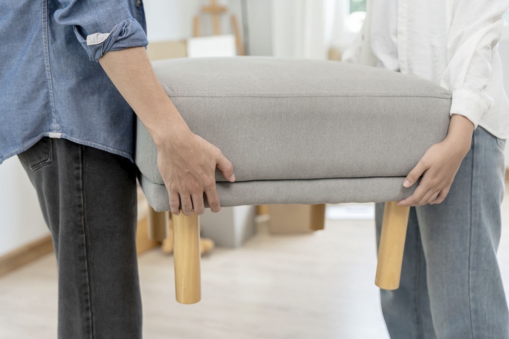 Мужчина и женщина несут небольшой пуфик в прихожею. 