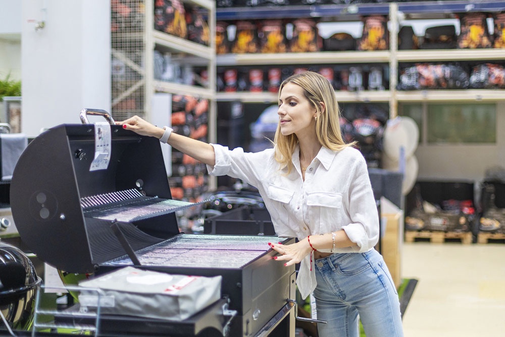 Женщина выбирает гриль в магазине для мужчины - подарок для любителя готовить на свежем воздухе.