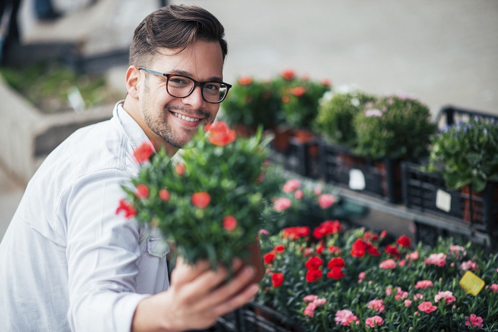 мужчина покупает цветы в горшочках.