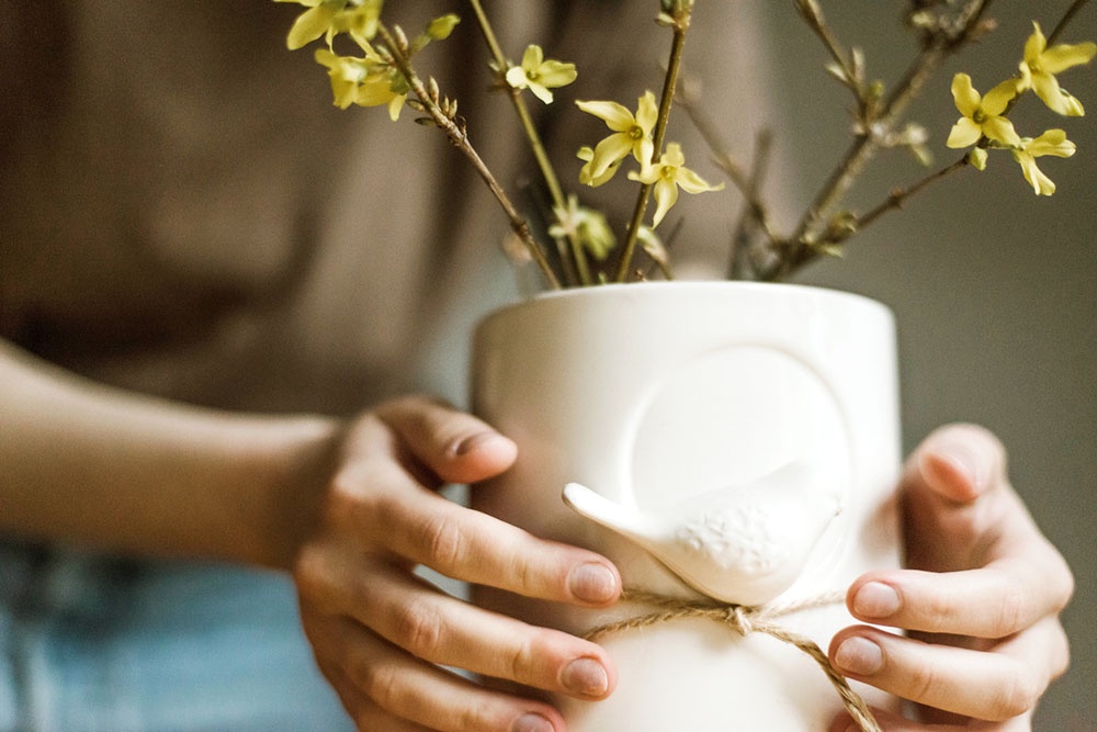 Женщина держит в руках  оригинальную  вазу с цветами.