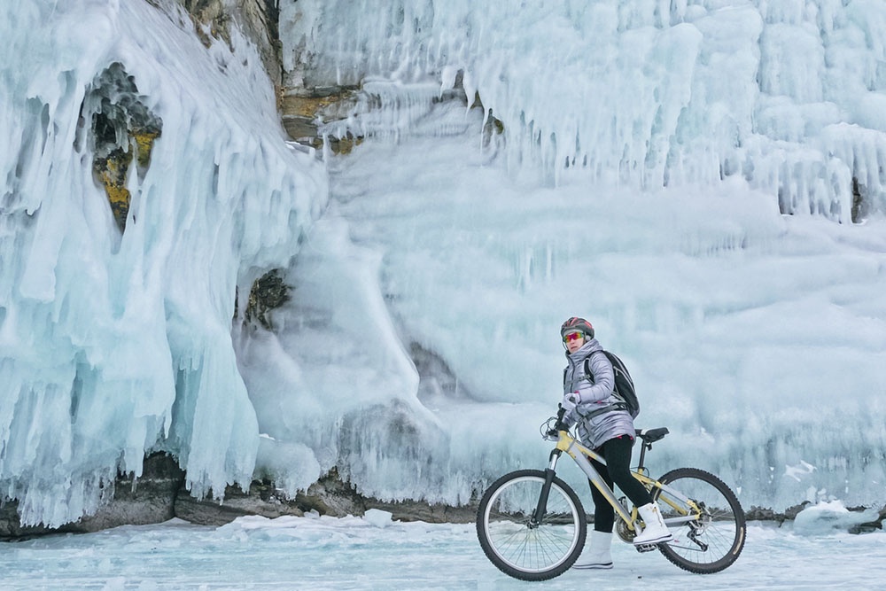 Женщина на велосипеде катается по прозрачному льду озера Байкал зимой. 