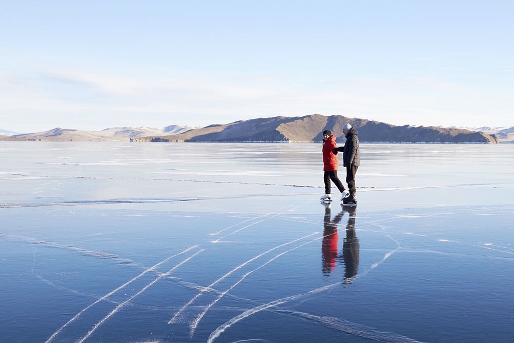 Пара катается на коньках по прозрачному льду озера Байкал зимой. 