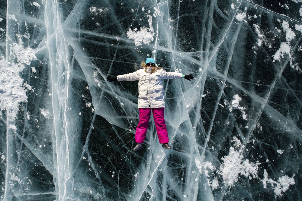 Человек на льду Байкала, застывшем в прозрачной тишине. Под ним - пузырьки метана, трещины и бесконечная глубина древнего озера.