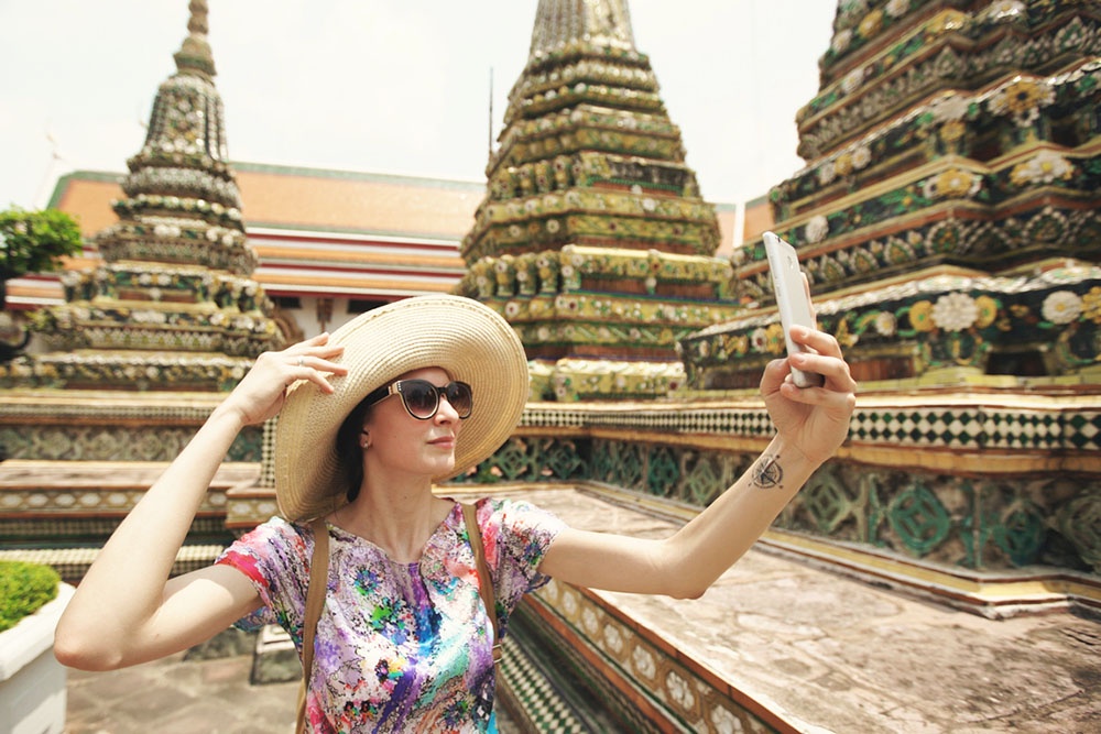 Туристка делает селфи у храма в Таиланде. Путешествие, достопримечательности, яркие эмоции в кадре.
