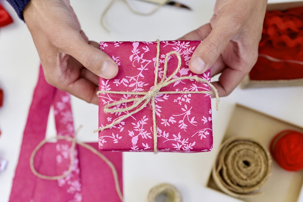 Мужчина упаковывает подарок в подарочную упаковку.