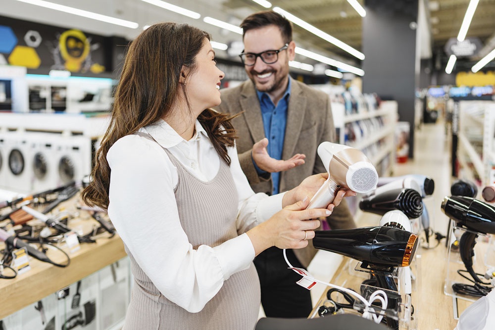 Муж покупает жене фен на 8 марта в магазине.