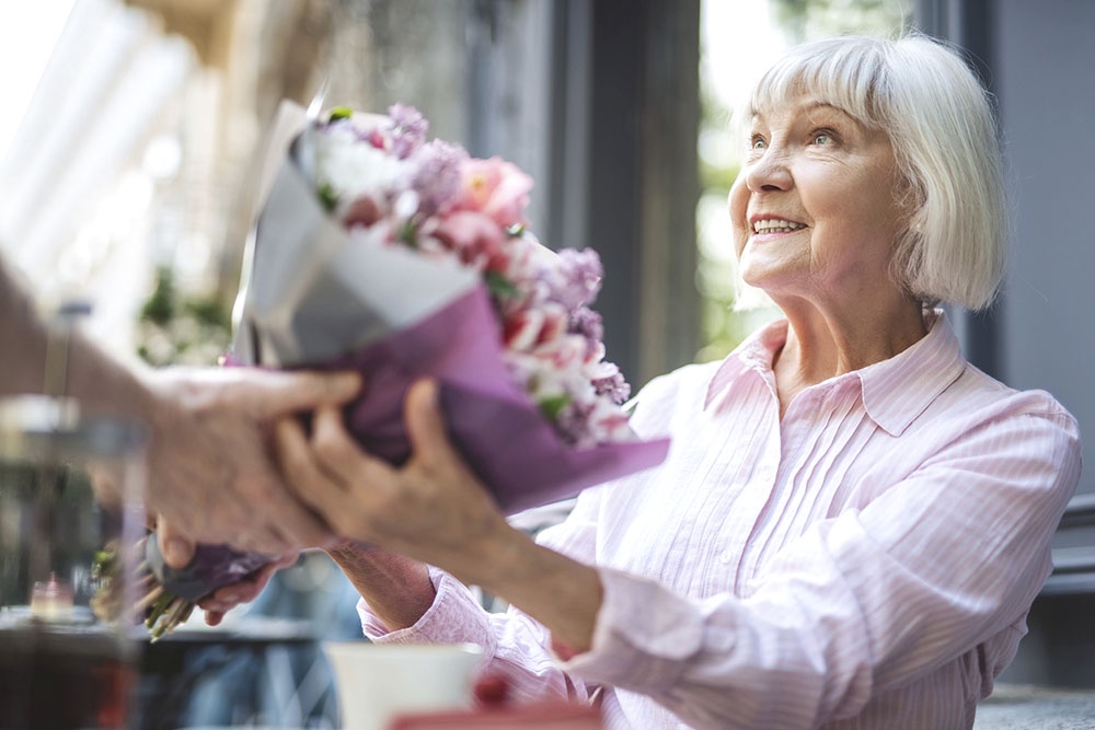 Поздравлять бабушку с 8 марта, дарит букет с цветами.