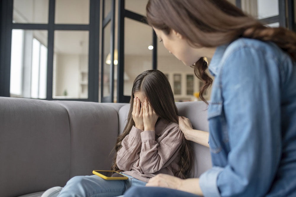 Мать утешает дочь, огорченную содержанием сообщения в телефоне.