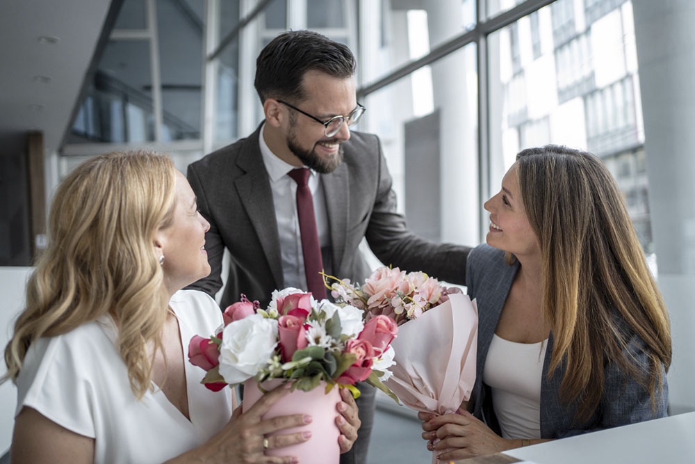 Мужчина поздравляет коллег с 8 марта, дарит букеты.