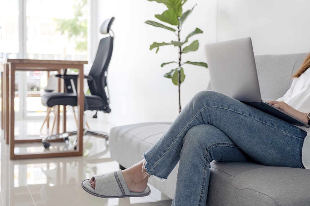 Женщина работает сидя на диване, игнорируя правильно организованное рабочее место.