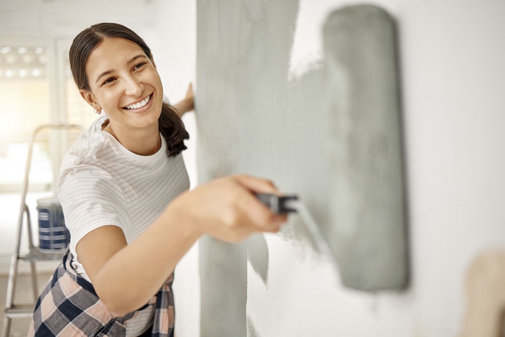 Девушка красит стены валиком дома.