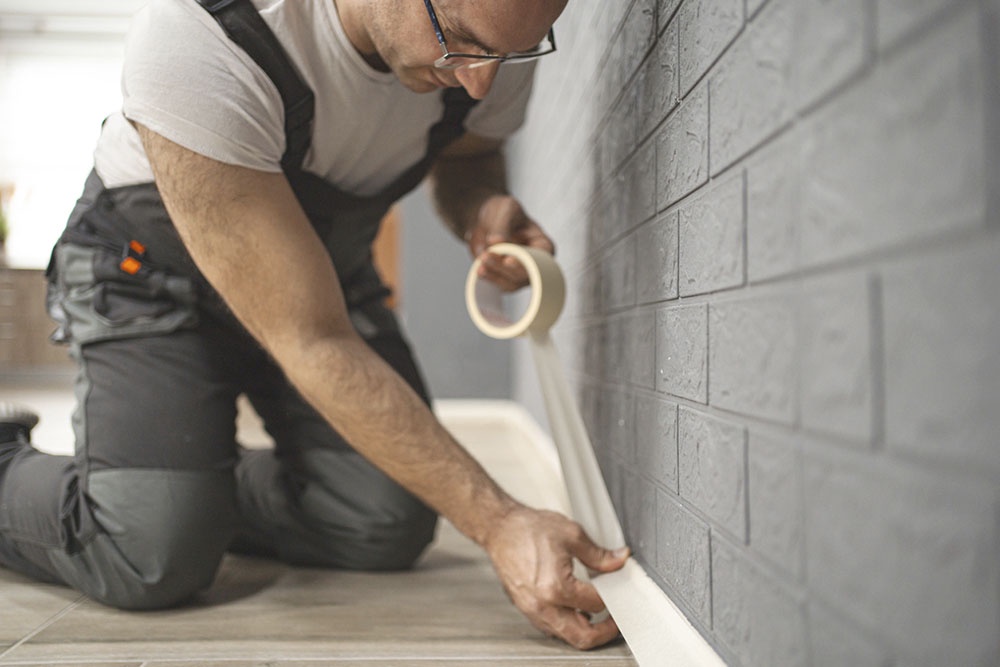 Мужчина заклеил плинтус малярным скотчем.