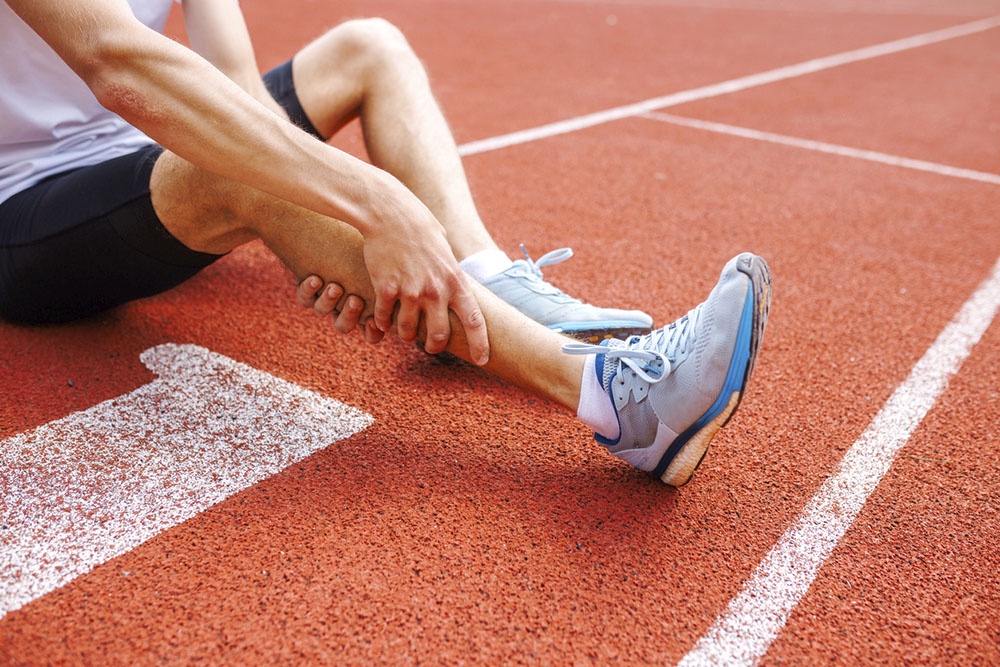Мужчина бегун, держится за травмированную голень.