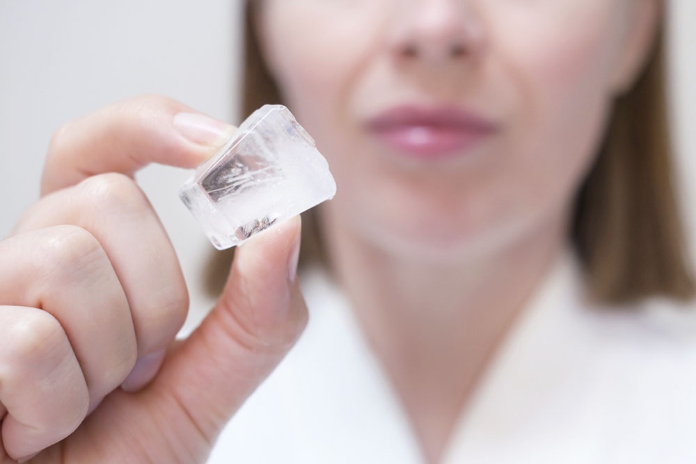 Женщина держит кусочек льда в руке, для домашних процедур.