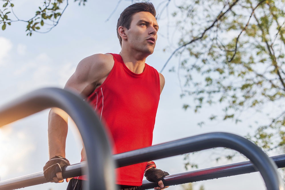 Мужчина в парке подтягивается на спортивных снарядах.