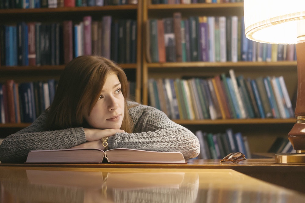 Девушка читает книгу с классическим романом в библиотеке.