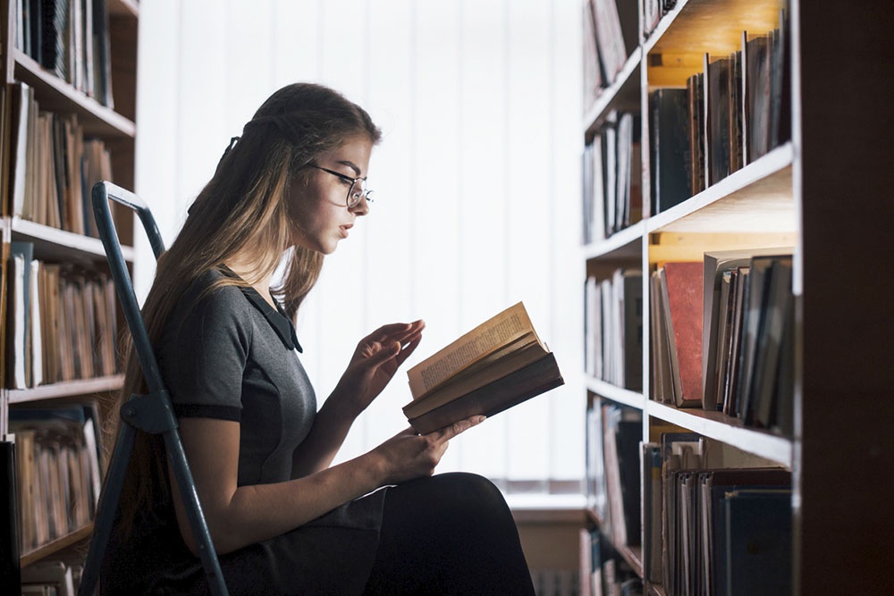 Девушка читает книгу с классическим романом в библиотеке.