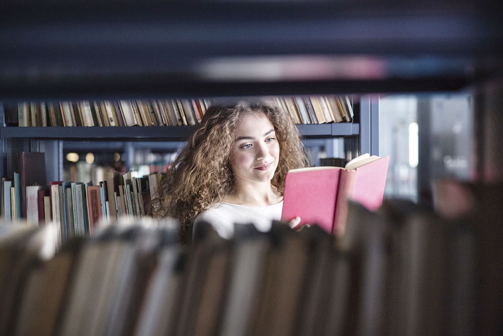 Девушка читает книгу с классическим романом в библиотеке.