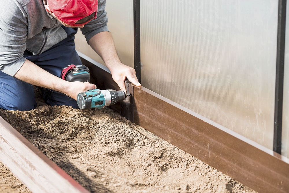 Мужчина собирает теплицу.