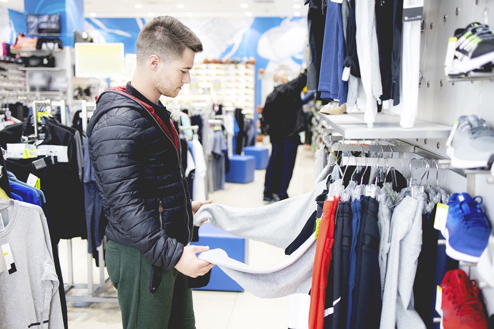 Мужчина выбирает одежду в спортивном магазине.