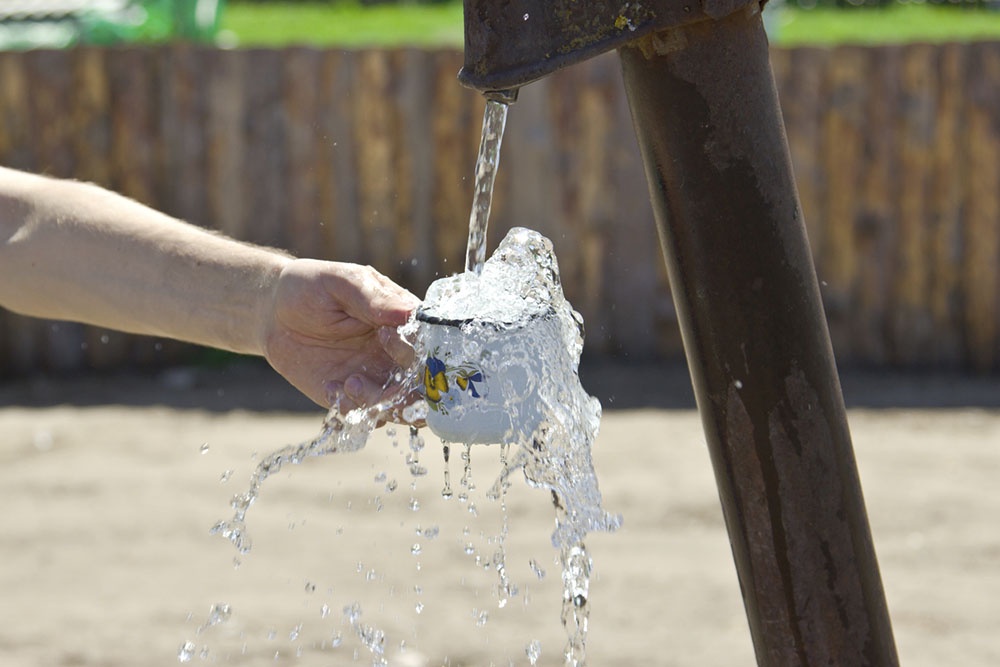 Человек набирает воду в кружку из колонки.