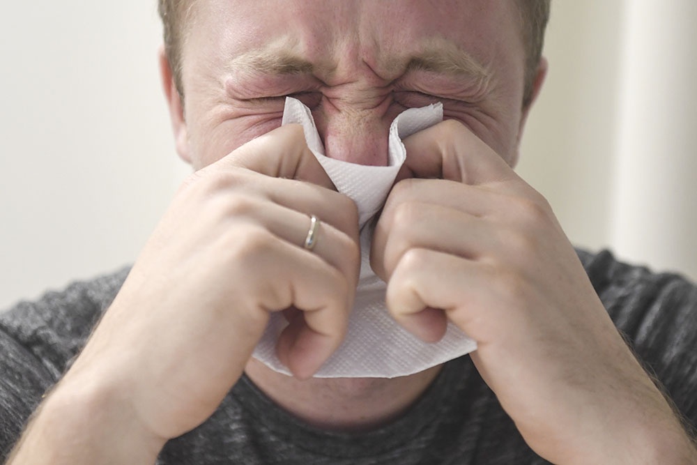 Мужчина с сильным насморком и покраснением кожи на лице, признаки аллергической реакции на пыльцу, поллиноз, аллергия на цветение трав.