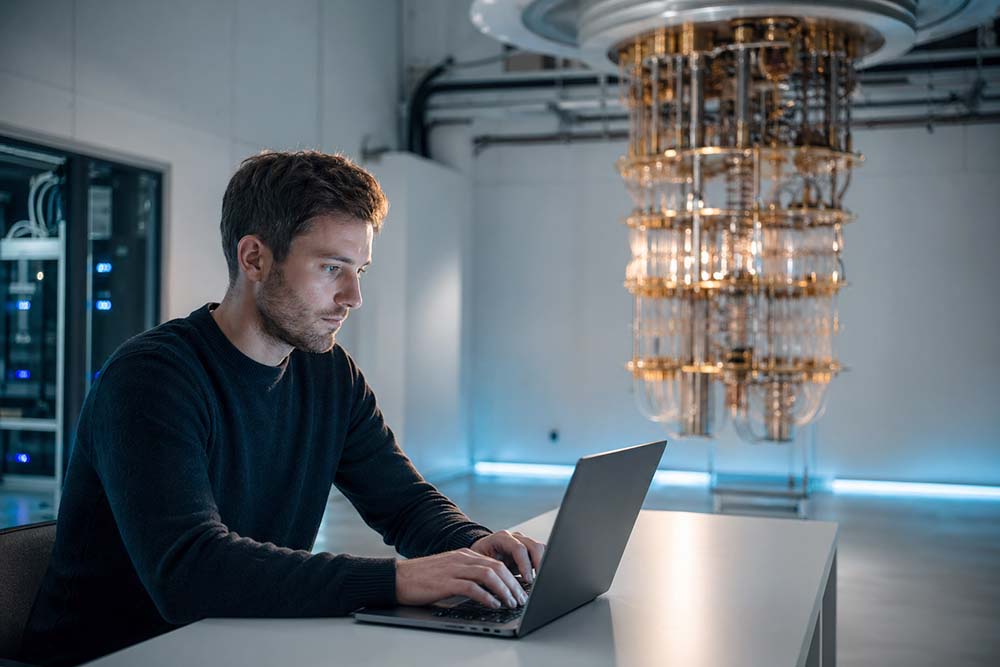 Сотрудник центра работает на ноутбуке. На дальнем плане - квантовый компьютер.