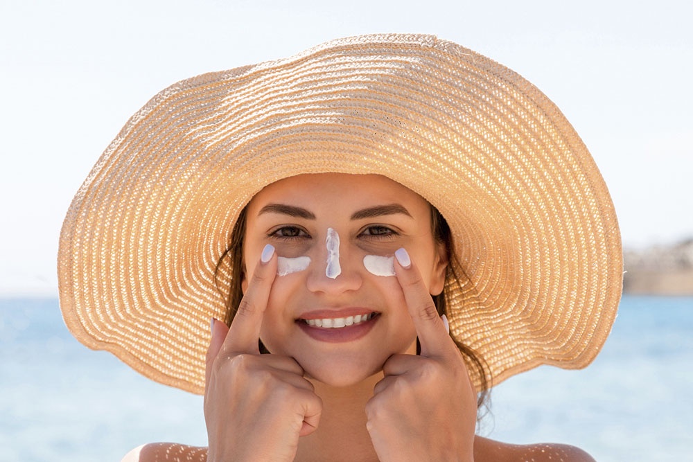 Девушка наносит солнцезащитный крем с SPF на лицо, защита в солнечный день.