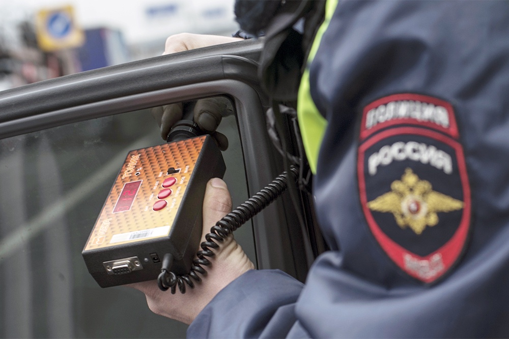 Руки полицейского держат прибор по измерению светопропускаемости тонировки на автомобиле