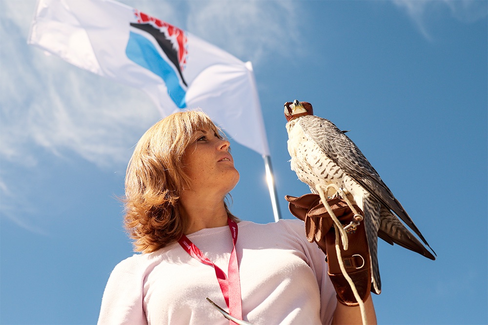 Женщина держит на руках сокола на фоне развивающегося флага