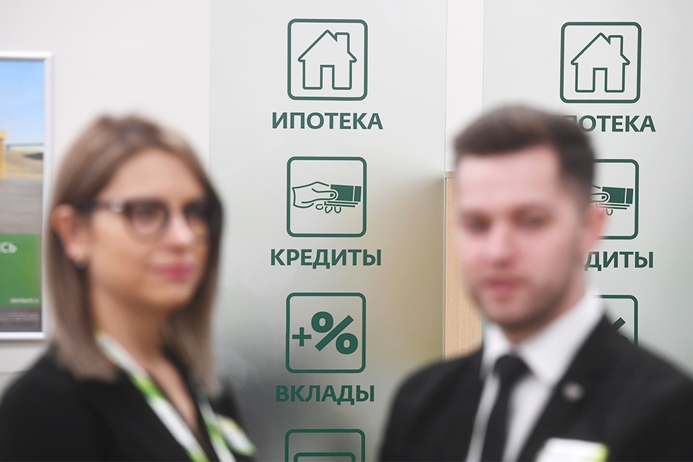 Сотрудники банка стоят возле стенда с информацией об ипотеке, кредитах и вкладах