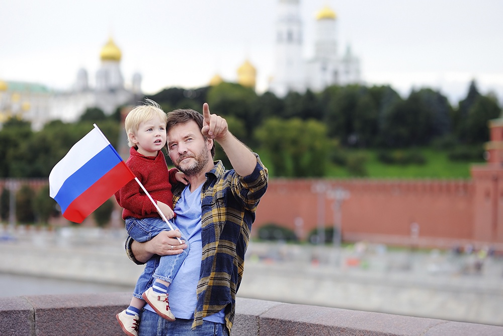 Папа с сыном в центре Москвы с российским флагом смотрят достопримечательности.