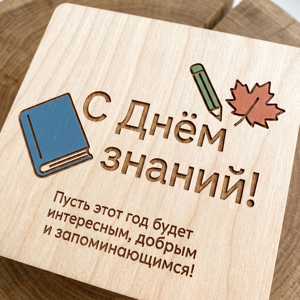 Деревянная открытка с книгой, кленовым листом и текстом: "С Днем знаний! Пусть этот год будет интересным, добрым и запоминающимся!"