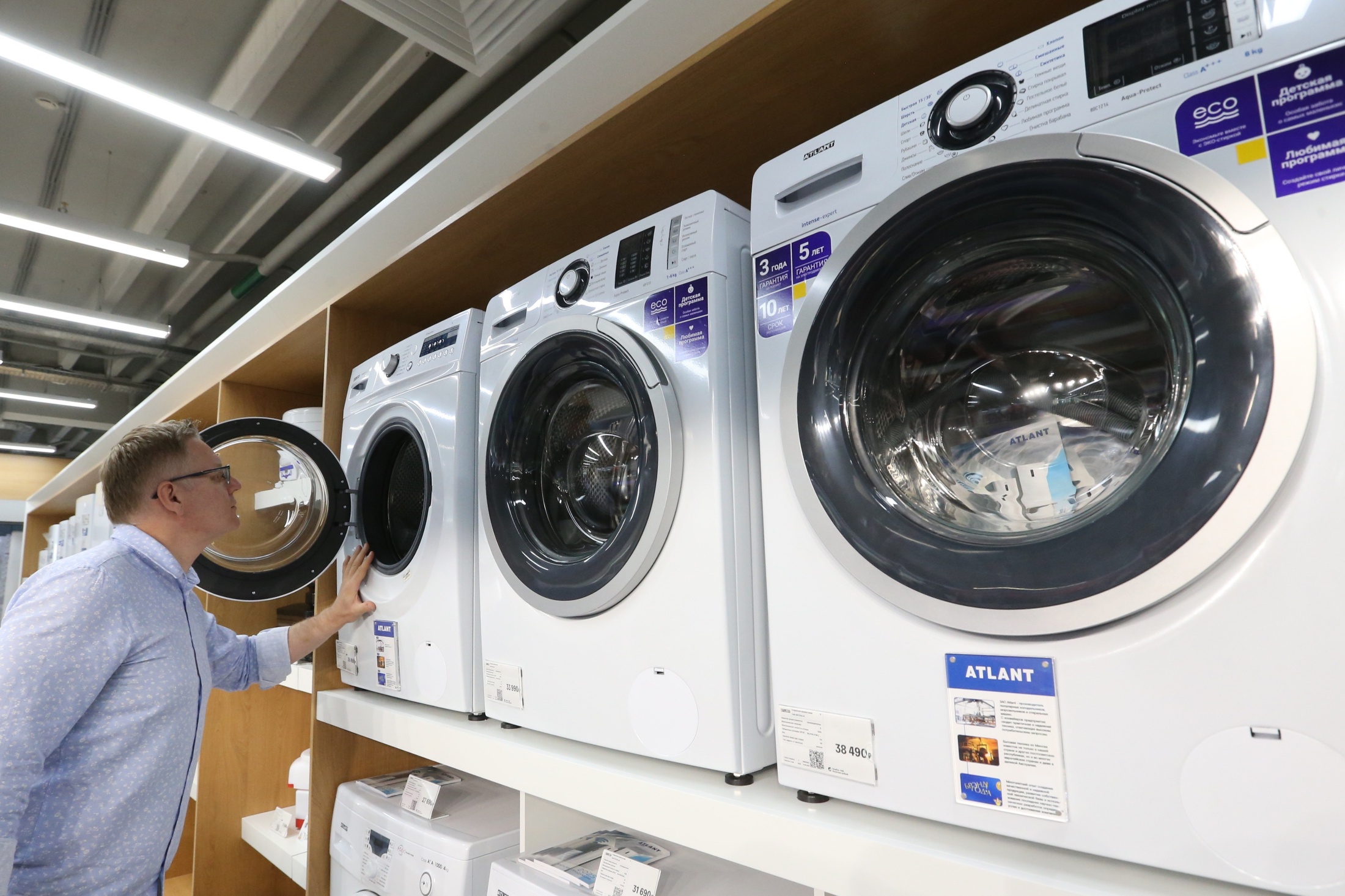 Покупатель выбирает стиральную машину в магазине бытовой техники, сравнивая модели и цены
