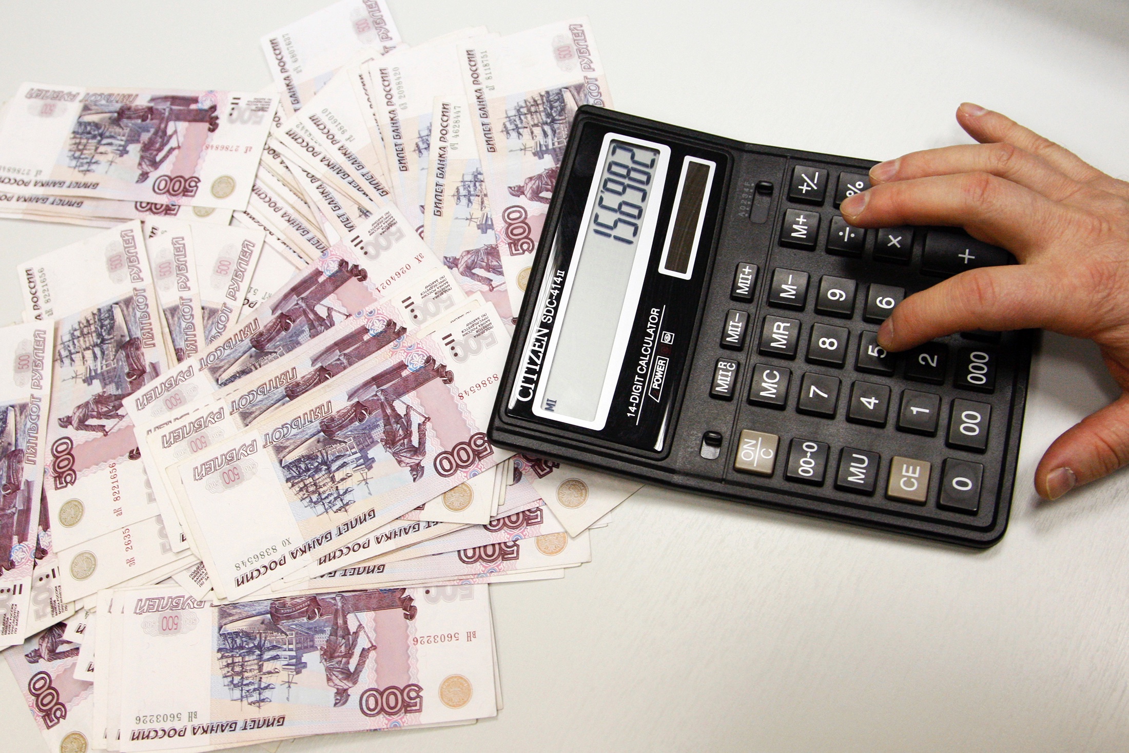 Мужчина считает на калькуляторе, рядом с которым лежат деньги