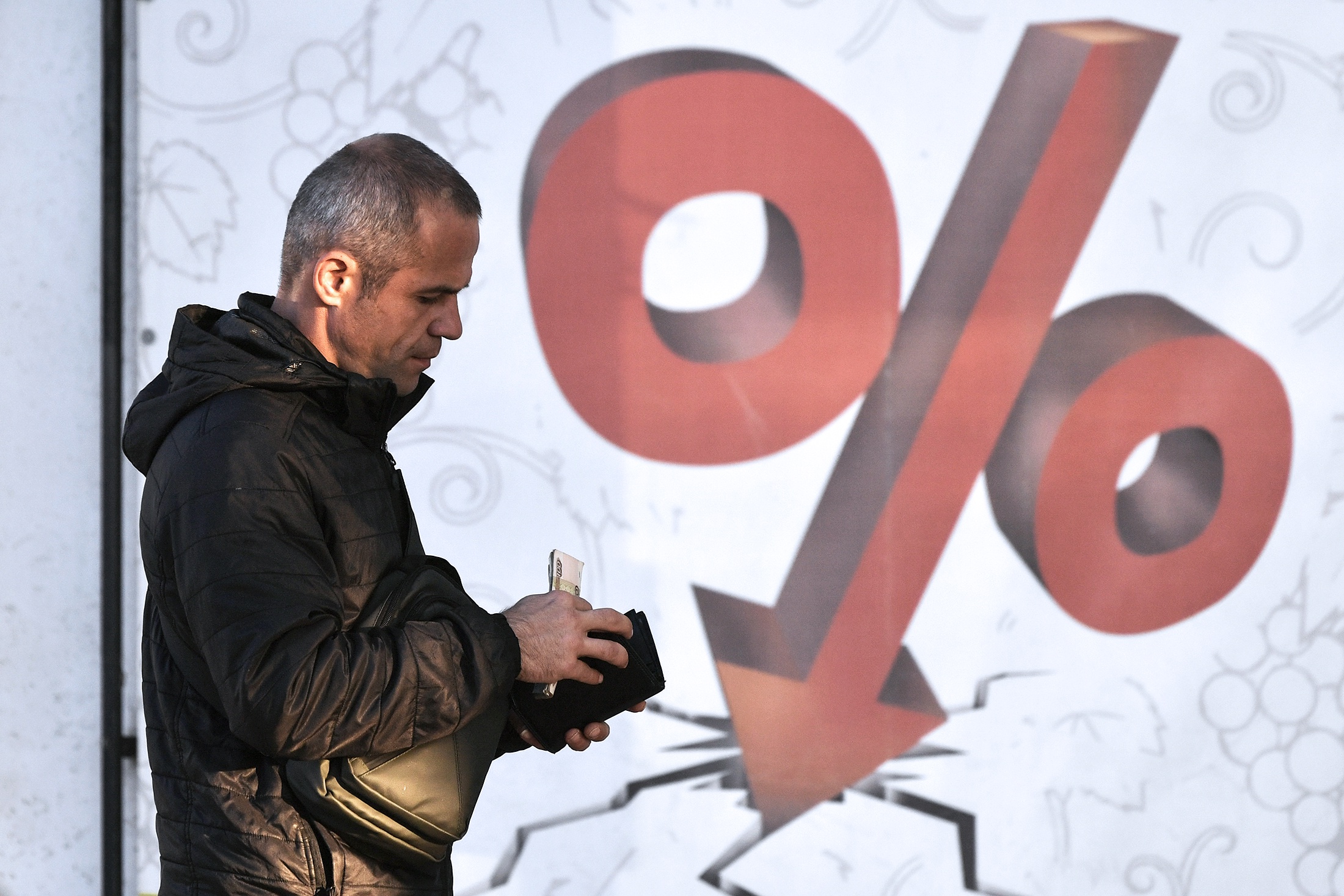 Мужчина убирает деньки в кошелек на фоне витрины с знаком проценты.