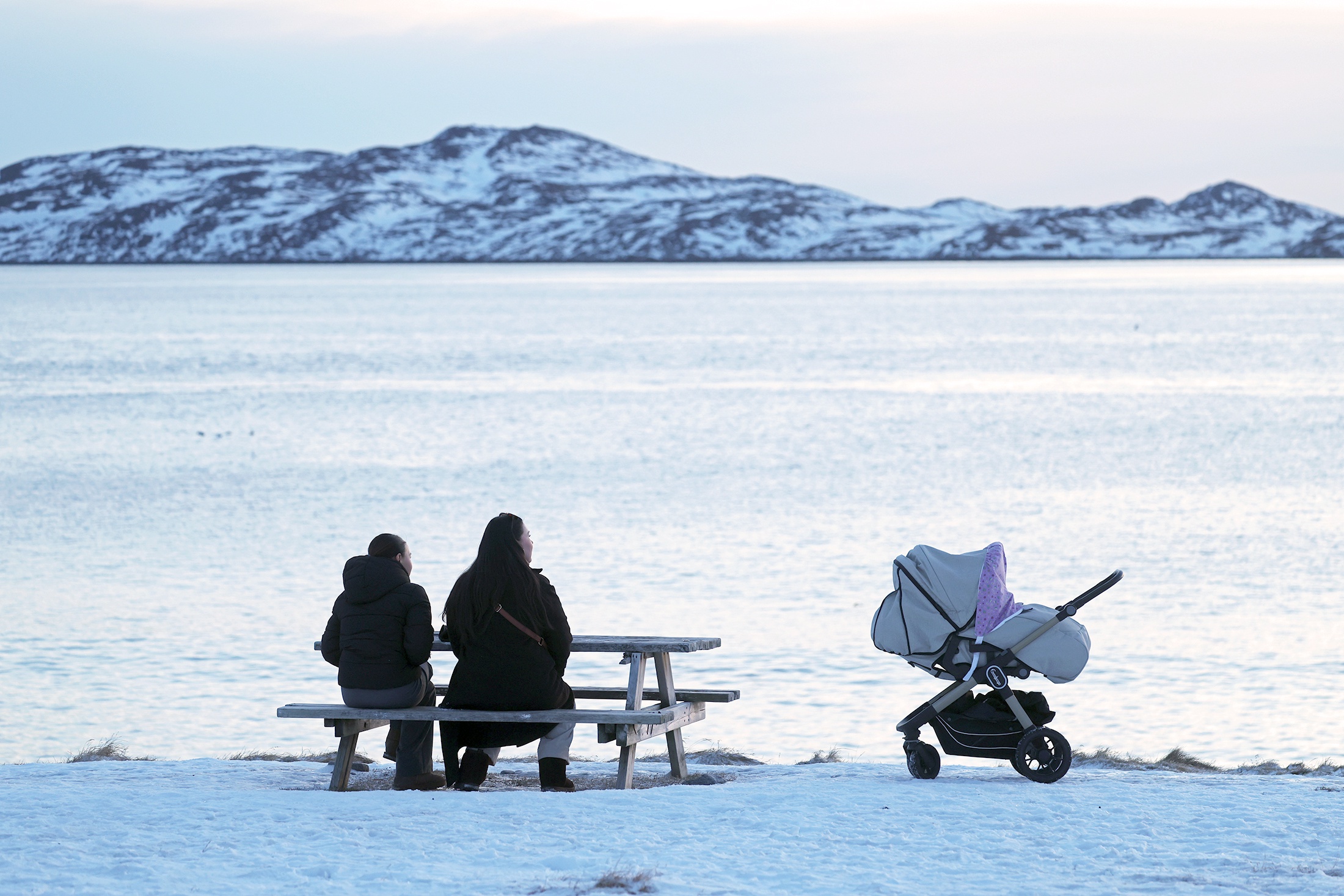Женщина и мальчик сидят на лавочке рядом с детской коляской у северного залива.