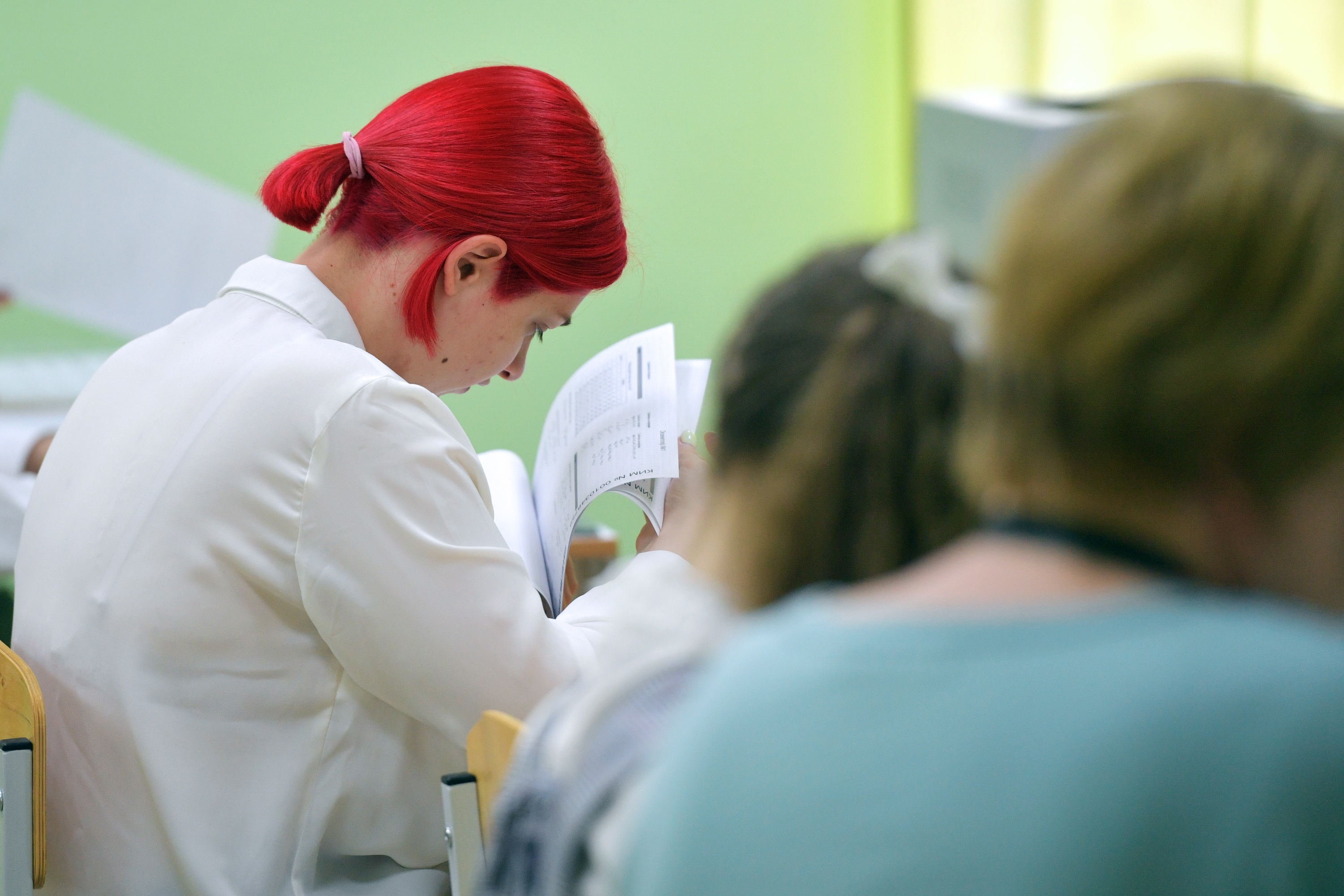 Девочка с красными волосами сидя смотрит задание по математике на листе бумаги. 