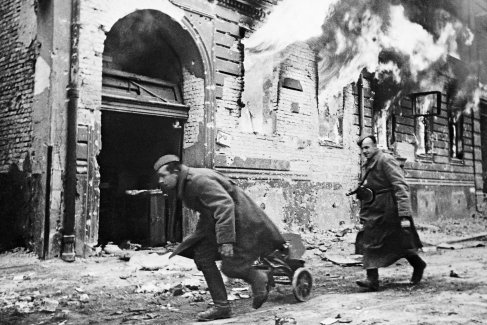 Советские пулеметчики продвигаются вдоль горящего здания на улице Берлина. 