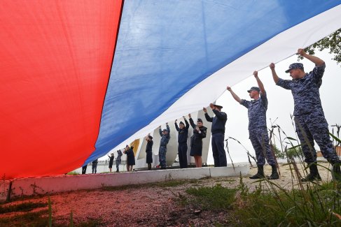 Сотрудники Федеральной службы судебных приставов, Росгвардии и полиции разворачивают полотно российского флага на Титовской сопке после автопробега в честь Дня флага Российской Федерации в Чите.