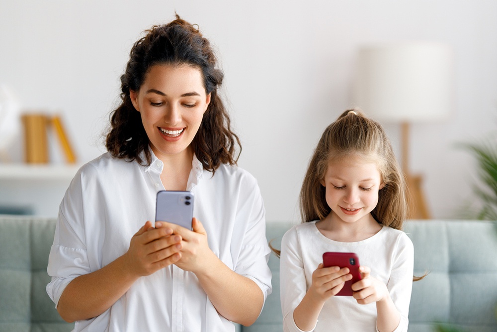 Мама и дочка сидят со смартфонами в руках.