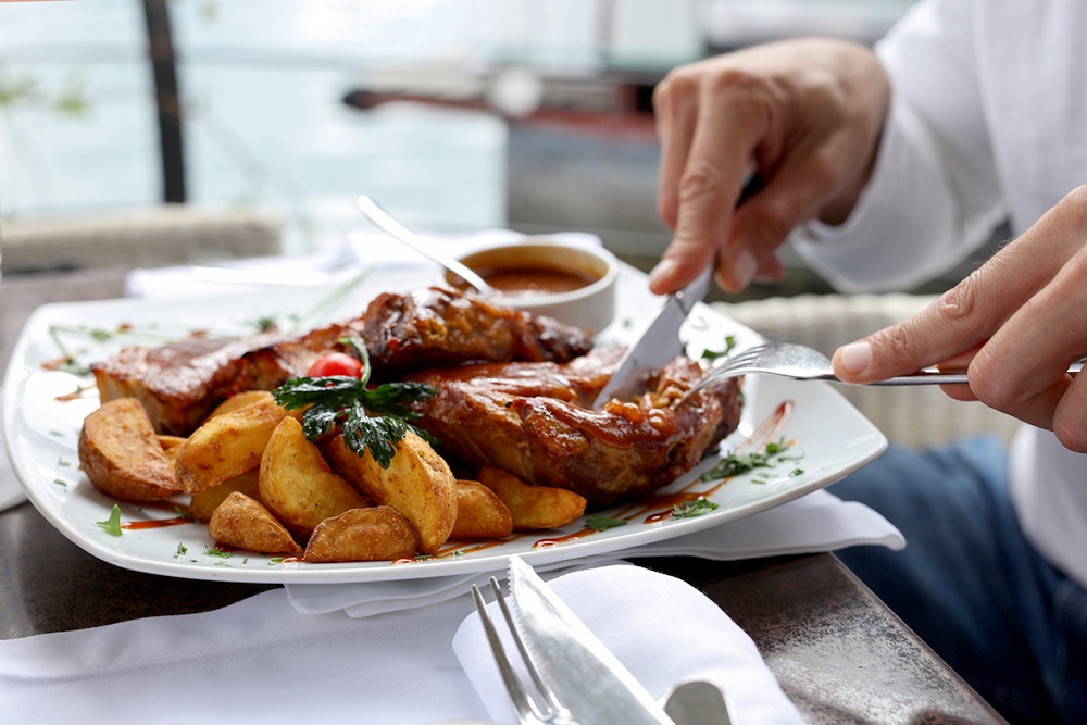 Мужчина режет мясо на тарелке